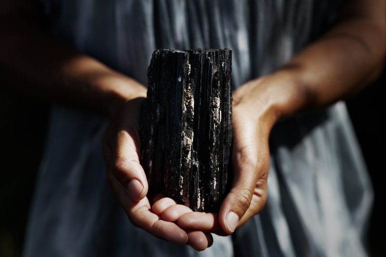 Hands holding a chunk of raw black tourmaline, one of the best crystals for protection