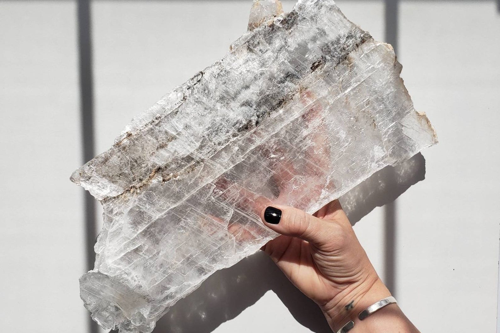 Large raw selenite slab held by a human hand in direct sunlight
