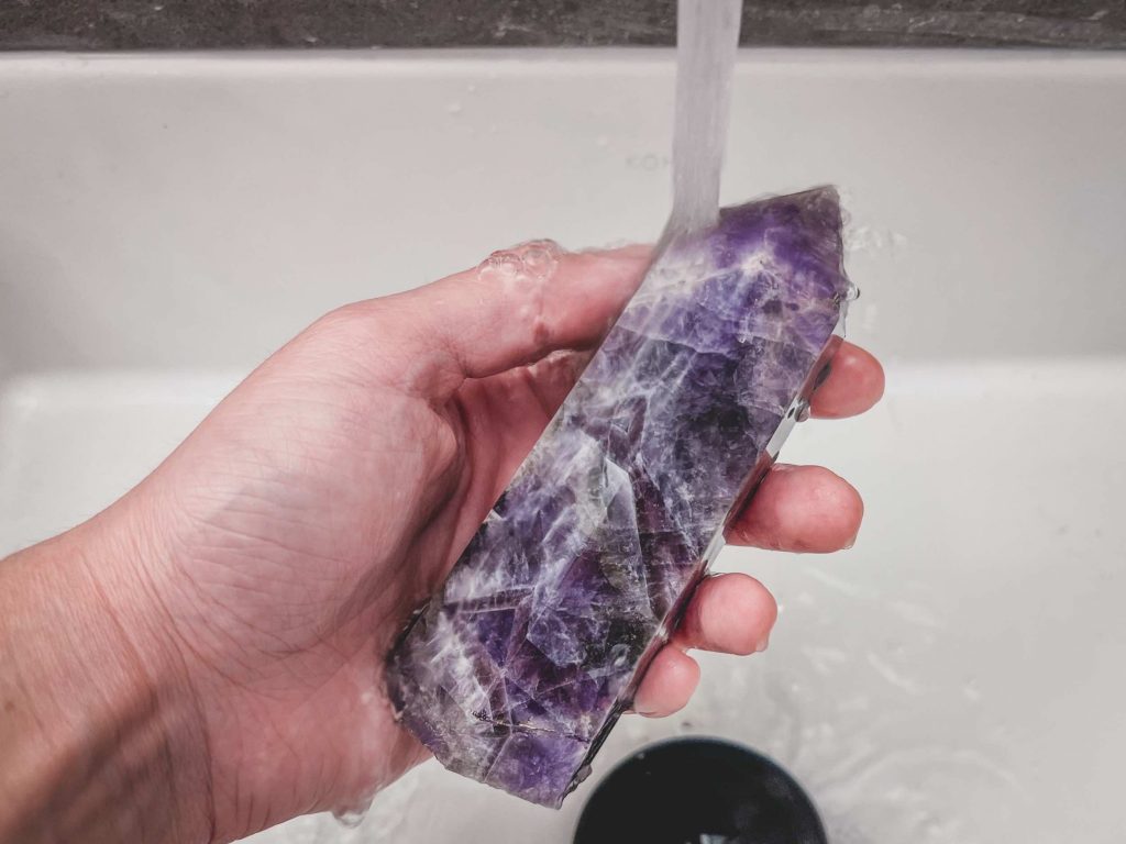 Amethyst crystal point cleansing under running tap water