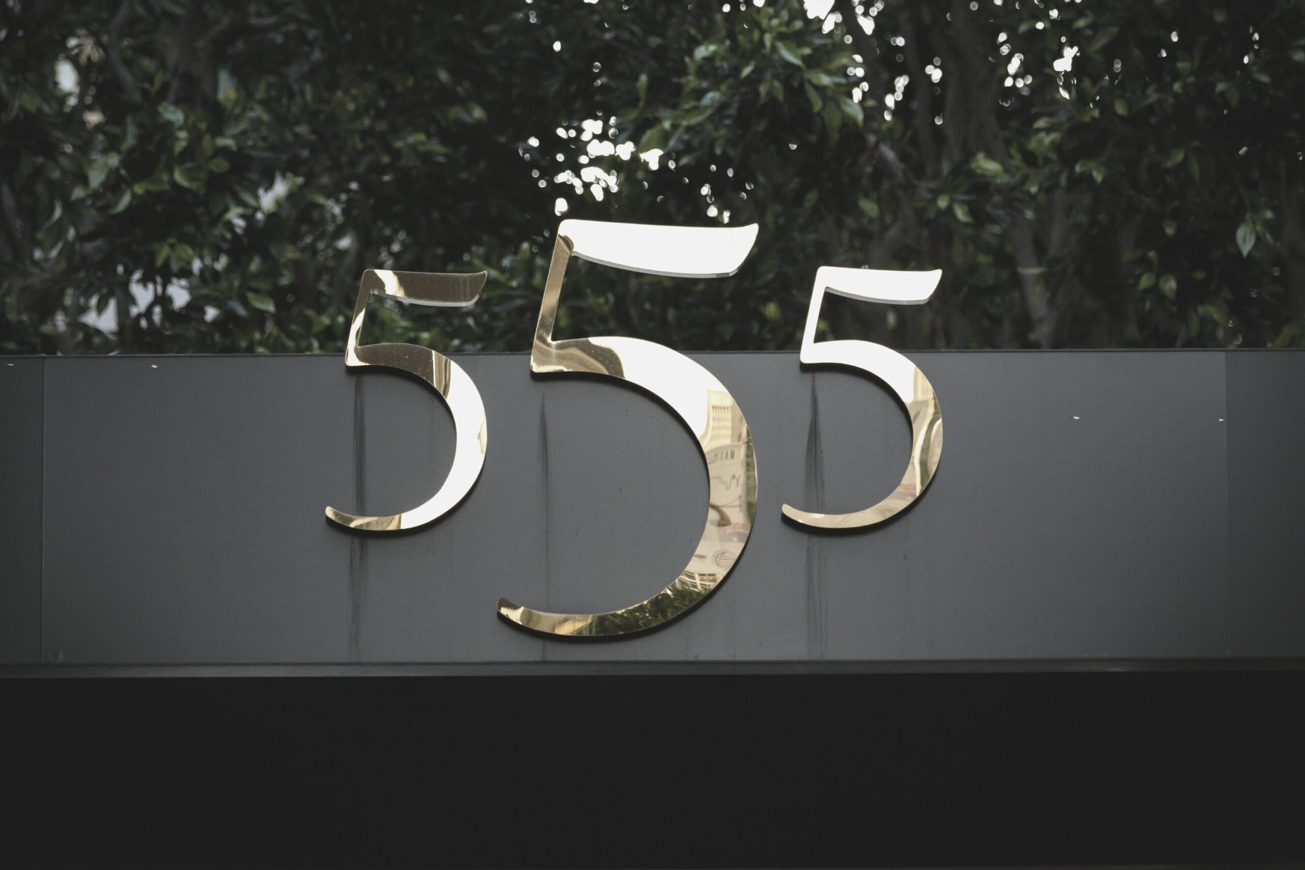 Photograph of the numbers 555 in shiny gold mounted on a building