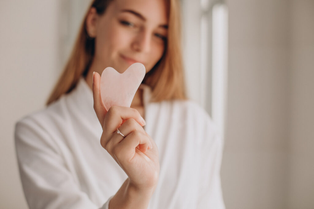 Woman holds up a gua sha massage stone, considering whether rose quartz can go in water