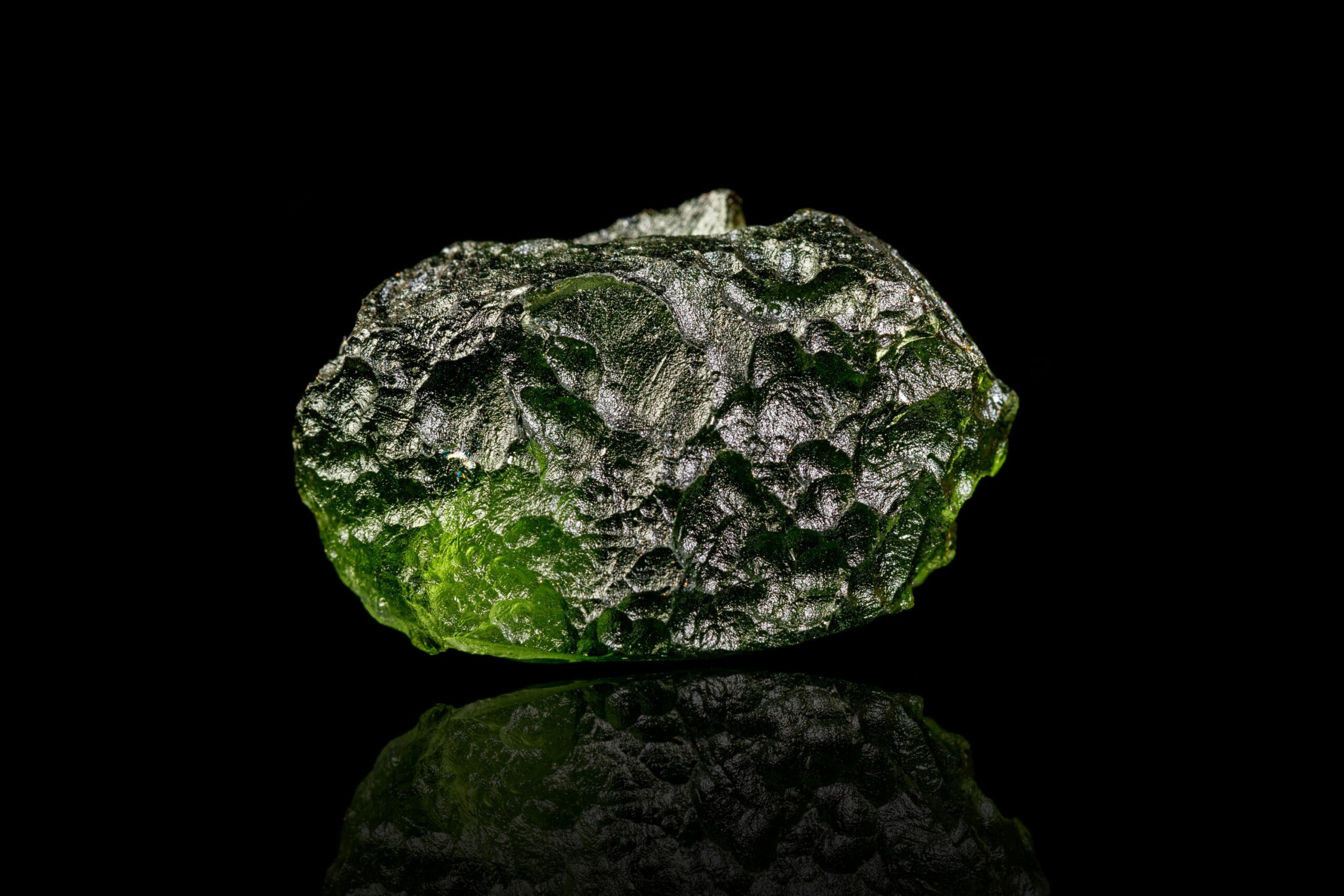 Green moldavite crystal on a reflective black surface